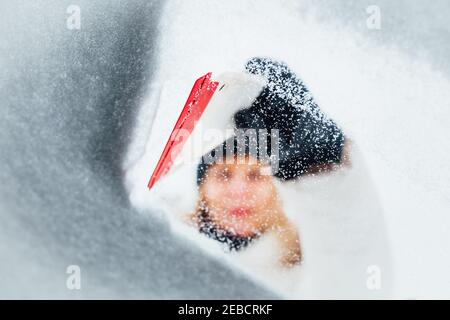 raschietto di plastica - una donna pulisce il vetro di una macchina in inverno dalla neve Foto Stock