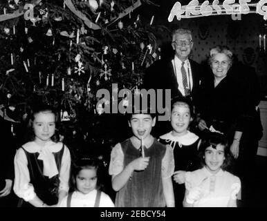 Accoglienza per le famiglie del personale della Casa Bianca. National Park Service (NPS) fotografo, Abbie Rowe (dietro a destra, con occhiali), e diverse persone non identificate si trovano di fronte all'albero di Natale nella Blue Room della Casa Bianca, Washington, D.C., durante un ricevimento per il personale e le loro famiglie. [Numeri scritti nell'angolo in alto a destra della stampa del contatto] Foto Stock