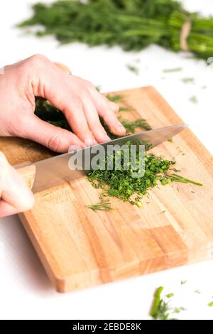 Le mani della donna tagliano l'aneto sul tagliere con un coltello bianco fondo cottura sping o l'atmosfera estiva Foto Stock