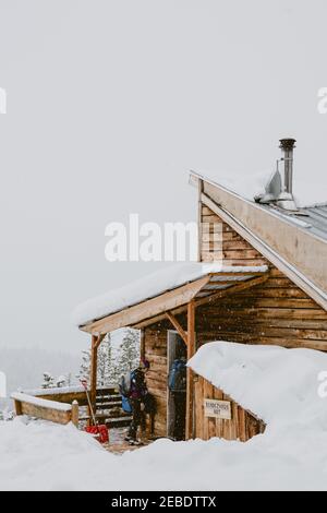 Due amici camminano in una cabina rustica mentre nevica esterno Foto Stock