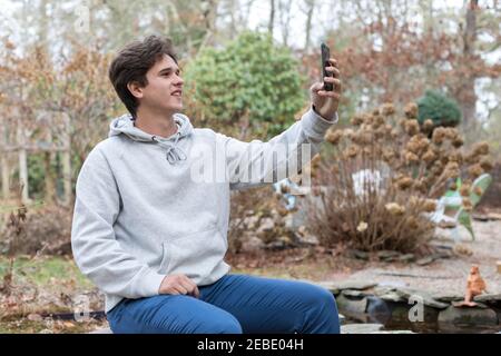 Studente di scuola maschile caucasica seduto all'aperto prendendo selfie Foto Stock