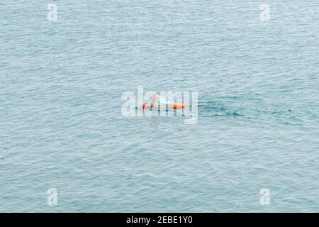 Nuotatore a lunga distanza con cappuccio arancione e borsa a secco in acqua oceano aperta senza fine Foto Stock