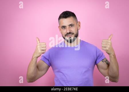 Giovane bell'uomo che indossa t-shirt casual su sfondo rosa segno di successo facendo gesto positivo con la mano, pollici su sorridente e felice. Ex allegro Foto Stock