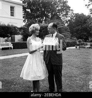 Piantando un cespuglio di rose alla Casa Bianca. Piantando un cespuglio di rose alla Casa Bianca. Donna non identificata presenta Assistente Speciale al Presidente Frederick G. Dutton con cartello per la Fiera della Contea di San Mateo (California) e Floral Fiesta. Ala est, Casa Bianca, Washington, D.C. Foto Stock