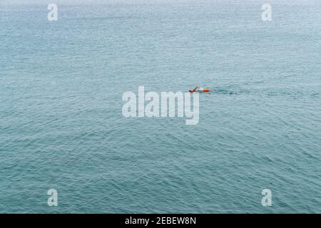 Nuotatore a lunga distanza con cappuccio arancione e borsa a secco in acqua oceano aperta senza fine Foto Stock