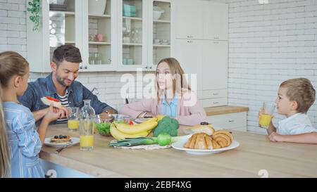 La famiglia parla durante la colazione vicino al cibo sul tavolo da cucina Foto Stock