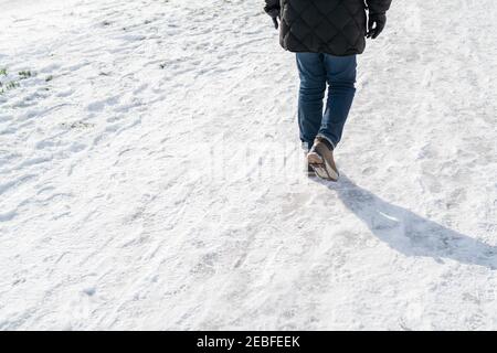 Uomo che cammina sulla neve compatta indossando sovrascarpe in gomma antiscivolo, con chiodi a vite per la presa Foto Stock