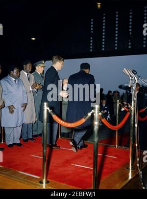 Cerimonia di arrivo per Kwame Nkrumah, presidente del Ghana, 15:43. Cerimonie di arrivo in onore del Presidente della Repubblica del Ghana, Osagyefo Dr. Kwame Nkrumah; il Presidente John F. Kennedy e il Presidente Nkrumah si preparano a scendere dalla piattaforma. Da sinistra a destra: Due uomini non identificati; il presidente dei capi di Stato congiunti, il generale Lyman Lemnitzer; il presidente Kennedy; il segretario di Stato, il dean Rusk; il presidente Nkrumah (di ritorno alla camera). Hangar n. 10, Terminal del Servizio militare di trasporto aereo (MATS), Aeroporto Nazionale di Washington, Washington, D.C. Foto Stock