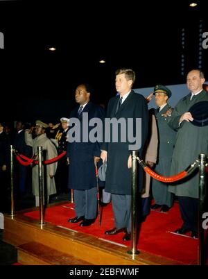 Cerimonia di arrivo per Kwame Nkrumah, presidente del Ghana, 15:43. Il presidente John F. Kennedy partecipa alle cerimonie di arrivo in onore del presidente della Repubblica del Ghana, Osagyefo Dr. Kwame Nkrumah. Sulla piattaforma (L-R): Presidente Nkrumah; Presidente Kennedy; Presidente dei Capi di Stato congiunti, Generale Lyman Lemnitzer; Segretario di Stato, Dean Rusk. Anche nella foto: Naval Aide al presidente, Comandante Tazewell Shepard. Hangar n. 10, Terminal del Servizio militare di trasporto aereo (MATS), Aeroporto Nazionale di Washington, Washington, D.C. Foto Stock