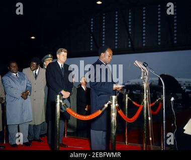 Cerimonia di arrivo per Kwame Nkrumah, presidente del Ghana, 15:43. Il presidente della Repubblica del Ghana, Osagyefo Dr. Kwame Nkrumah, fa commenti alle cerimonie di arrivo in suo onore. Da sinistra a destra: Due uomini non identificati; il presidente dei capi di Stato congiunti, il generale Lyman Lemnitzer (parzialmente nascosto); il presidente John F. Kennedy; il segretario di Stato, Dean Rusk (dietro il braccio del presidente Kennedyu2019s); l'ufficiale di protocollo per il dipartimento di Stato, Clement E. u0022Clemu0022 Conger; il presidente Nkrumah (ai microfoni). Hangar n. 10, terminal dei servizi di trasporto aereo militare (MATS), aeroporto nazionale di Washington, W. Foto Stock