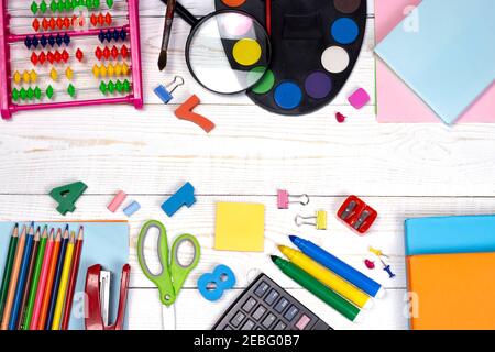 Composizione di posa di un appartamento di ritorno a scuola. Forniture scolastiche, matite, pitture, forbici, lenti d'ingrandimento e libri colorati, sul tavolo bianco con copia spac Foto Stock