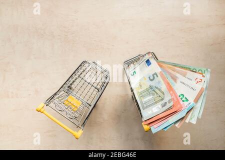 Carrello pieno di banconote in valuta europea e un altro vuoto sullo sfondo con spazio per la copia. Due carrelli - vuoti e con banconote in euro. T Foto Stock