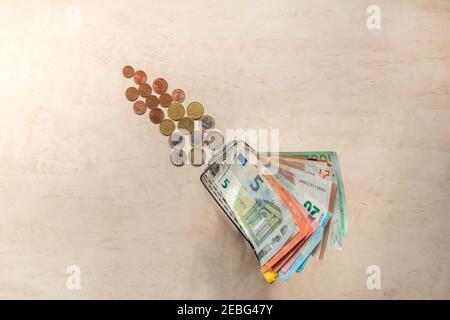Banconote in euro in piccolo carrello e monete in euro sullo sfondo. Carrello per lo shopping in miniatura con contanti. Denaro dell'area dell'euro. Spazio di copia. Vista dall'alto. Ho Foto Stock