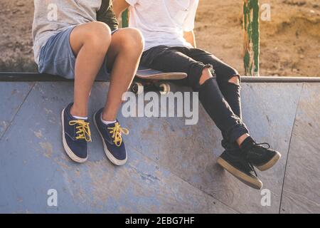 In prossimità dei due giovani ragazzi seduti sul mezzo tubo rampa, dopo Nizza trucchi e salti al skatepark. Alla moda di adolescenti godendo il tempo libero al pattino p Foto Stock