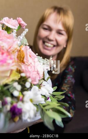 Defocalizzare la donna sorridente. Bella donna bionda di mezza età che si sente entusiasta di ricevere un bel bouquet di fiori per le vacanze di primavera. San Valentino, madri Foto Stock