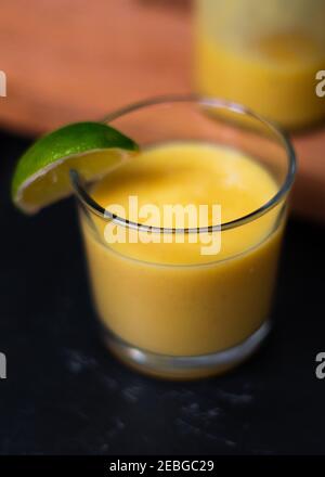 Un angolo di primo piano rivolto verso il basso su un succo di frutta o un frullato in un bicchiere con un segmento di lime sul lato. Vasetto o bottiglia di succo sullo sfondo. Forte v Foto Stock