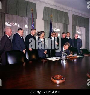 Firma della proclamazione - Voluntary Overseas Aid Week, 11:30. Il presidente John F. Kennedy (seduto) firma la proclamazione che designa la settimana del 9 aprile 1962, come settimana volontaria di aiuti esteri. I leader delle organizzazioni umanitarie e religiose americane guardano avanti. In piedi, (L-R): Non identificato; Richard W. Reuter, Direttore Esecutivo DELLA CURA; Fowler Hamilton, Amministratore dell'Agenzia per lo sviluppo Internazionale (in dietro, per lo più nascosto); Dr. Franklin Clark Fry, Presidente del Lutheran World Relief; Joseph Meyerhoff, Presidente Generale dell'appello Ebraico Unito; Segretario dell'Agricoltura Orville L. F. Foto Stock