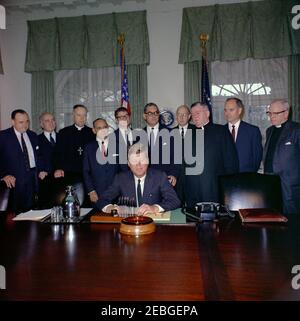 Firma della proclamazione - Voluntary Overseas Aid Week, 11:30. Il presidente John F. Kennedy (seduto) fa un commento alla firma della proclamazione che designa la settimana del 9 aprile 1962 come settimana volontaria degli aiuti esteri. I leader delle organizzazioni umanitarie e religiose americane guardano avanti. In piedi, (L-R): Richard W. Reuter, Direttore Esecutivo DELLA CURA; Fowler Hamilton, Amministratore dell'Agenzia per lo sviluppo Internazionale; Dr. Franklin Clark Fry, Presidente del Lutheran World Relief; Joseph Meyerhoff, Presidente Generale dell'appello ebraico Unito; Segretario dell'Agricoltura Orville L. Freeman; Ra Foto Stock