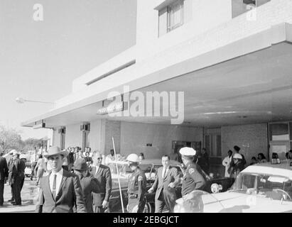 Viaggio in Texas: Parkland Hospital (esterno); limousine Presidentu2019s; Love Field, corpo del Presidentu2019s portato su Air Force One. Ufficiali di polizia e astanti si riuniscono di fronte a un ingresso al Parkland Hospital di Dallas, Texas, dopo l'arrivo della limousine presidenziale che porta il presidente John F. Kennedy. Al centro si trova Malcolm Kilduff, segretario alla stampa. Foto Stock