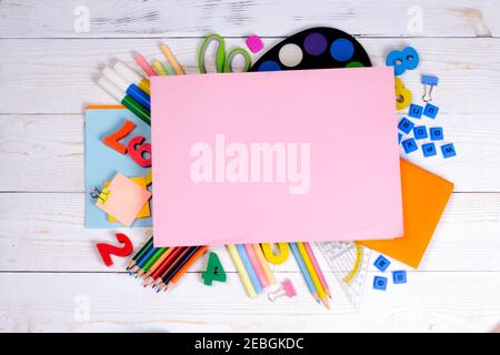 Bianco di carta rosa e forniture scolastiche su sfondo di legno bianco. Concetto di ritorno a scuola con spazio di copia per testo piatto, vista dall'alto, mockup. Foto Stock