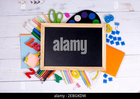 lavagna con gesso e forniture scolastiche su sfondo di legno bianco. Concetto di ritorno a scuola con spazio di copia per testo piatto, vista dall'alto, mockup. Foto Stock