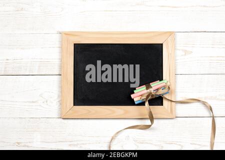 Lavagna e gessetti colorati con nastro su sfondo di legno bianco con spazio per la copia per testo piatto, vista dall'alto, mockup. Foto Stock