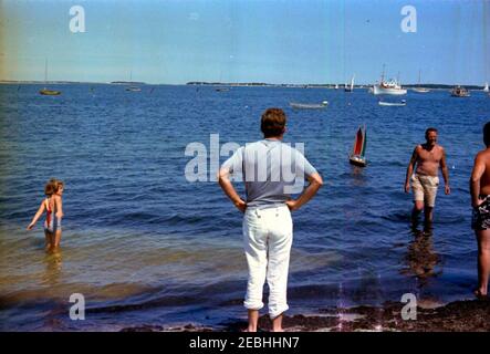 Week-end Independence Day a Hyannis Port: Lancio di John F. Kennedy, Jr. 0027s giocattolo a vela (dono del presidente italiano segni) con Caroline Kennedy (CBK), Edward M. Kennedy (EMK), e K. LeMoyne (u201cLemu201d) Billings. Il presidente John F. Kennedy (al centro, girato indietro) guarda il lancio di John F. Kennedy, Jr. U0027s barca a vela giocattolo a Hyannis Port, Massachusetts, durante l'Independence Day Weekend. Anche nella foto (L-R): Caroline Kennedy; l'amico di famiglia Kennedy, Kirk LeMoyne u201cLemu201d Billings; e il senatore Edward M. Kennedy del Massachusetts (sull'estremità più a destra della cornice, indietro girato). Foto Stock