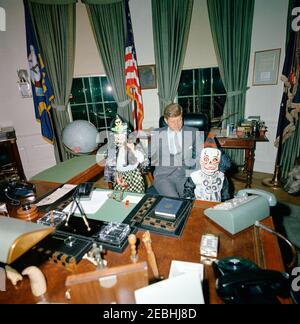 Il presidente Kennedy con Caroline Kennedy (CBK) u0026 John F. Kennedy, Jr. (JFK, Jr.), in costumi di Halloween. Il presidente John F. Kennedy visita con i suoi figli, Caroline Kennedy (a sinistra, con un gatto) e John F. Kennedy, Jr., nell'Ufficio ovale; i bambini indossano i costumi di Halloween. Il cane della famiglia Kennedy, Wolf, è visibile sul bordo più a destra del telaio. White House, Washington, D.C. Foto Stock