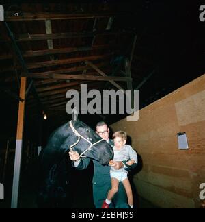 Caroline Kennedy (CBK) u0026 John F. Kennedy, Jr. (JFK, Jr.), presso Fort Myer Stables. John F. Kennedy, Jr. (Tenuto da un uomo non identificato), alimenta un cavallo durante una visita alle scuderie di Fort Myer ad Arlington, Virginia. Foto Stock