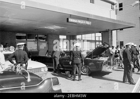 Viaggio in Texas: Parkland Hospital (esterno); limousine Presidentu2019s; Love Field, corpo del Presidentu2019s portato su Air Force One. Gli agenti di polizia si riuniscono intorno alla limousine presidenziale (Lincoln-Mercury Continental) di fronte ad un ingresso al Parkland Hospital di Dallas, Texas, dopo l'arrivo del presidente John F. Kennedy. Foto Stock