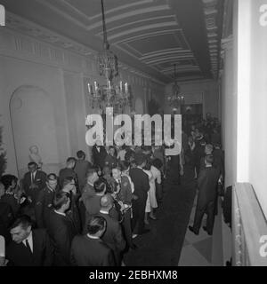White House staff Christmas Party nella East Room, 18:30. Il presidente John F. Kennedy e la First Lady Jacqueline Kennedy (entrambi in centro sullo sfondo, visti dall'alto) accolgono gli ospiti riuniti a Cross Hall, durante una festa di Natale per il personale della Casa Bianca; i membri del personale riempiono il corridoio che conduce alla Sala da pranzo di Stato. Anche nella foto: Militare Aide al presidente generale Chester V. Clifton; primo segretario sociale Ladyu2019s, Letitia Baldrige; fotografo del National Park Service (NPS), Abbie Rowe; White House Secret Service agenti, Clint Hill e Toby Chandler. White House, Washington, D.C. Foto Stock