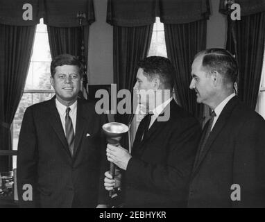 Il presidente pone per le fotografie con George McGovern e Joe Foss per l'uso all'apertura dei campionati di pista della National Association of InterCollegiate Athletics (NAIA) a Sioux Falls, South Dakota, 17:27. Il presidente John F. Kennedy visita con il commissario della American Football League e l'ex governatore del South Dakota, Joseph Foss (centro), e il direttore del Food for Peace e l'ex rappresentante del South Dakota, George McGovern (destra). Il sig. Foss possiede una torcia simbolica, consegnata a lui dal presidente Kennedy, che porterà a Sioux Falls, South Dakota, per aprire l'Associazione Nazionale di Foto Stock