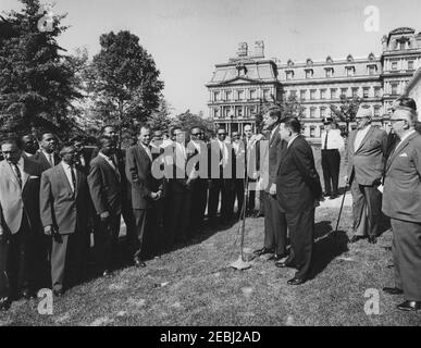Visita dei partecipanti all'American Institute for Free Labor Management, ore 10:05. Il presidente John F. Kennedy (ai microfoni) trasmette osservazioni ai partecipanti al programma di formazione dell'American Institute for Free Labour Development (AIFLD) per i leader sindacali dell'America Latina e dei Caraibi. Specialista America Latina del Dipartimento del lavoro degli Stati Uniti, Joaquin A. Bazan, Jr., si trova a destra del presidente Kennedy; partecipante Eric Lloyd Harris, della Giamaica (in dietro, parzialmente nascosto), si trova a sinistra del presidente. In piedi a destra (L-R): Presidente della Federazione americana del lavoro e del Congresso di Foto Stock