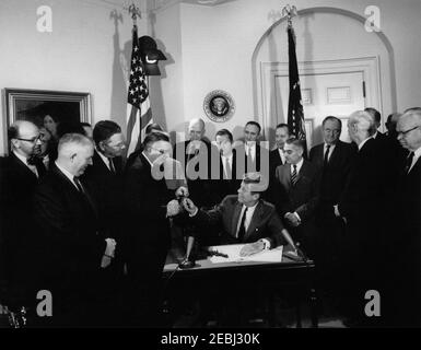 Firma della fattura - S.R. 11970 Legge pubblica 87-794, Legge di espansione di commercio di 1962, 12:10. Il presidente John F. Kennedy (seduto) distribuisce le penne dopo aver firmato il Trade Expansion Act del 1962. In piedi (L-R): Non identificato; Presidente del Comitato per una politica commerciale nazionale (CNTP), Carl J. Gilbert (in dietro, per lo più nascosto); Rappresentante John J. Flynt, Jr. (Georgia); Rappresentante Hale Boggs (Louisiana); Rappresentante Wilbur D. Mills dell'Arkansas (ricevendo una penna dal Presidente Kennedy); Senatore Robert S. Kerr (Oklahoma); Rappresentante John W. Byrnes (Wisconsin); senatore Mike Mansfield (Montana); Sen Foto Stock