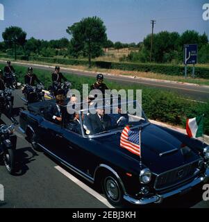 Viaggio in Europa: Italia, Napoli: Moto, 17:40. Il presidente John F. Kennedy giace sul sedile posteriore di un convertibile aperto mentre la sua motocicletta viaggia attraverso Napoli, Italia. Antonio segni, presidente d'Italia, siede con il presidente Kennedy. L'agente White House Secret Service, Gerald A. u201cJerryu201d Behn, si trova nel sedile centrale anteriore. Un accompagnatore di moto viaggia con l'auto. Foto Stock