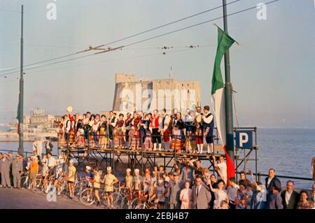 Viaggio in Europa: Italia, Napoli: Moto, 17:40. Le folle costeggiano la strada mentre il motociclista del presidente John F. Kennedyu2019s viaggia attraverso Napoli, Italia; il Castel dellu2019Ovo e il Golfo di Napoli sono visibili sullo sfondo. [Il graffio in basso al centro è originale al negativo.] Foto Stock