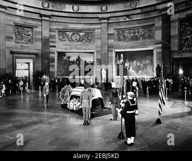 Funerale di Stato del presidente Kennedy: Giacere nello stato al Campidoglio degli Stati Uniti, partenza della famiglia Kennedy. Il defunto presidente John F. Kennedy si trova nello stato nella rotonda del Campidoglio degli Stati Uniti; il casket del presidente Kennedyu2019s con bandiera si trova al centro a sinistra. I membri della guardia d'onore stand orologio, tra cui il tenente William F. Lee; lutto file nella stanza da sinistra. Washington, D.C. Foto Stock