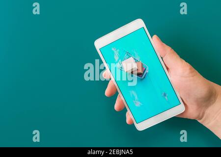 Immagine di carrelli vuoti e completi dello shopping sullo schermo del telefono che tengono in mano su sfondo turchese. Immagine mockup dello smartphone che tiene la mano con lo shopping Foto Stock