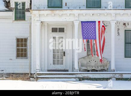 Bandiera americana infranto appesa verticalmente sul portico anteriore di una vecchia casa Foto Stock