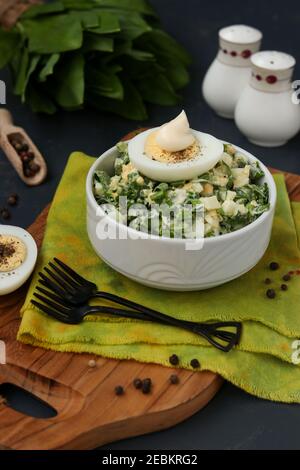 Insalata con aglio selvatico ramson, uova e maionese in una ciotola bianca su una tavola di legno Foto Stock