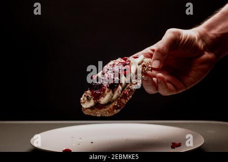 Sana colazione uomo brinda con marmellata di frutti di bosco, burro di arachidi al cioccolato, banana, zucca, girasole e semi di lino, sesamo, bacche di goji in una mano. Spazio di copia Foto Stock