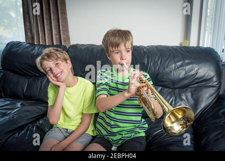 Due bambini seduti su un divano. Uno sta suonando una tromba e l'altro bambino sta ascoltando e sorridendo. Foto Stock