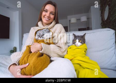 Donna in felpa accogliente con i suoi gatti che si sentono freddi e. riscaldamento sotto coperte Foto Stock