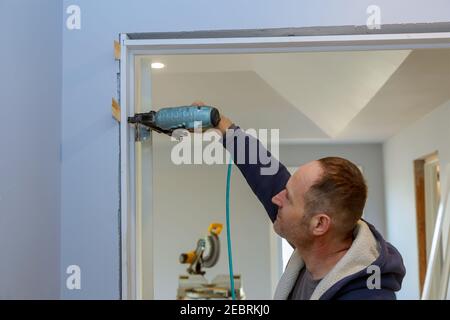 Installazione di una casa incompiuta una nuova porta interna in legno nel utilizzando un chiodo a pistola ad aria nella chiodatura per il lavoro di finitura Foto Stock