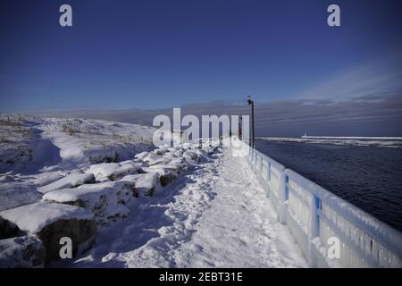 Grand Haven, Michigan, febbraio 2021, ringhiere e lampioni ricoperti di ghiaccio, lungo il sentiero innevato del molo, acqua invernale Foto Stock