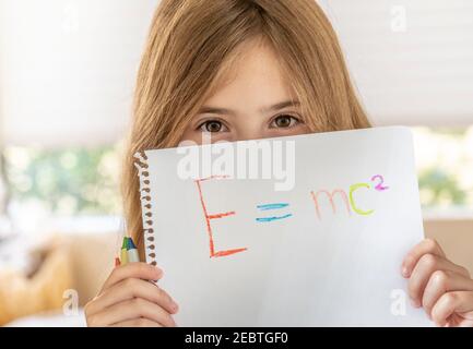 Ragazza (8-9) che tiene carta con formula Emc2 di fronte faccia Foto Stock