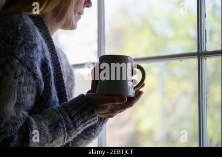 Donna che tiene la tazza e guarda fuori la finestra Foto Stock