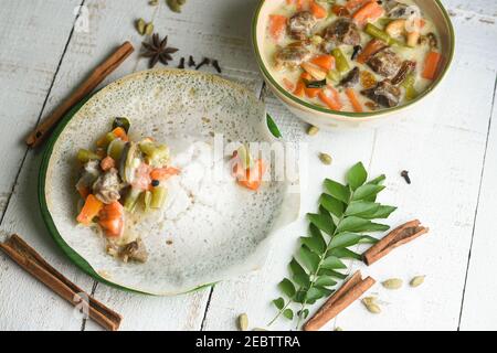 Stufato di mutton, zuppa di pollo stufato piatto laterale per Appam, pane, cibo per la colazione Kerala. Cibo indiano. Christian Natale cibo donna mano prendere curry piccante Foto Stock