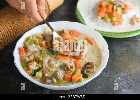 Stufato di mutton, zuppa di pollo stufato piatto laterale per Appam, pane, cibo per la colazione Kerala. Cibo indiano. Christian Natale cibo donna mano prendere curry piccante Foto Stock