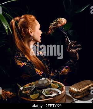 Ricca donna dai capelli rossi sta mangiando nel ristorante di pesce ha un gamberetti a forcella o langoutine al buio Foto Stock